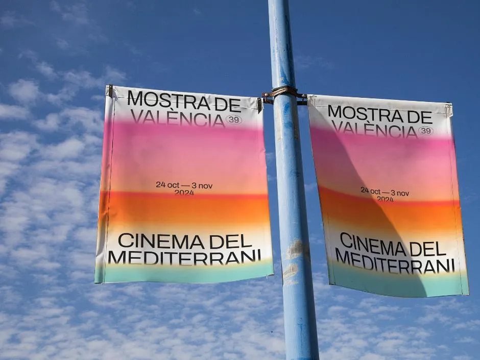 Dos banderolas de la Mostra de València colgadas de una farola contra el cielo